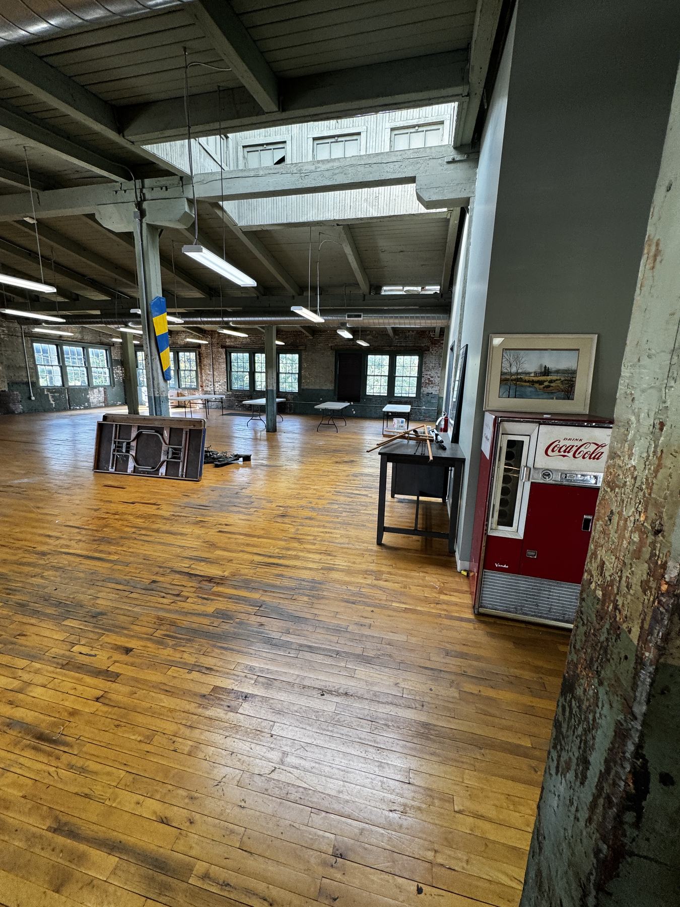 The room looking across open plank floor towards brick walls and windows, with a vintage Coca-Cola machine against the near wall.