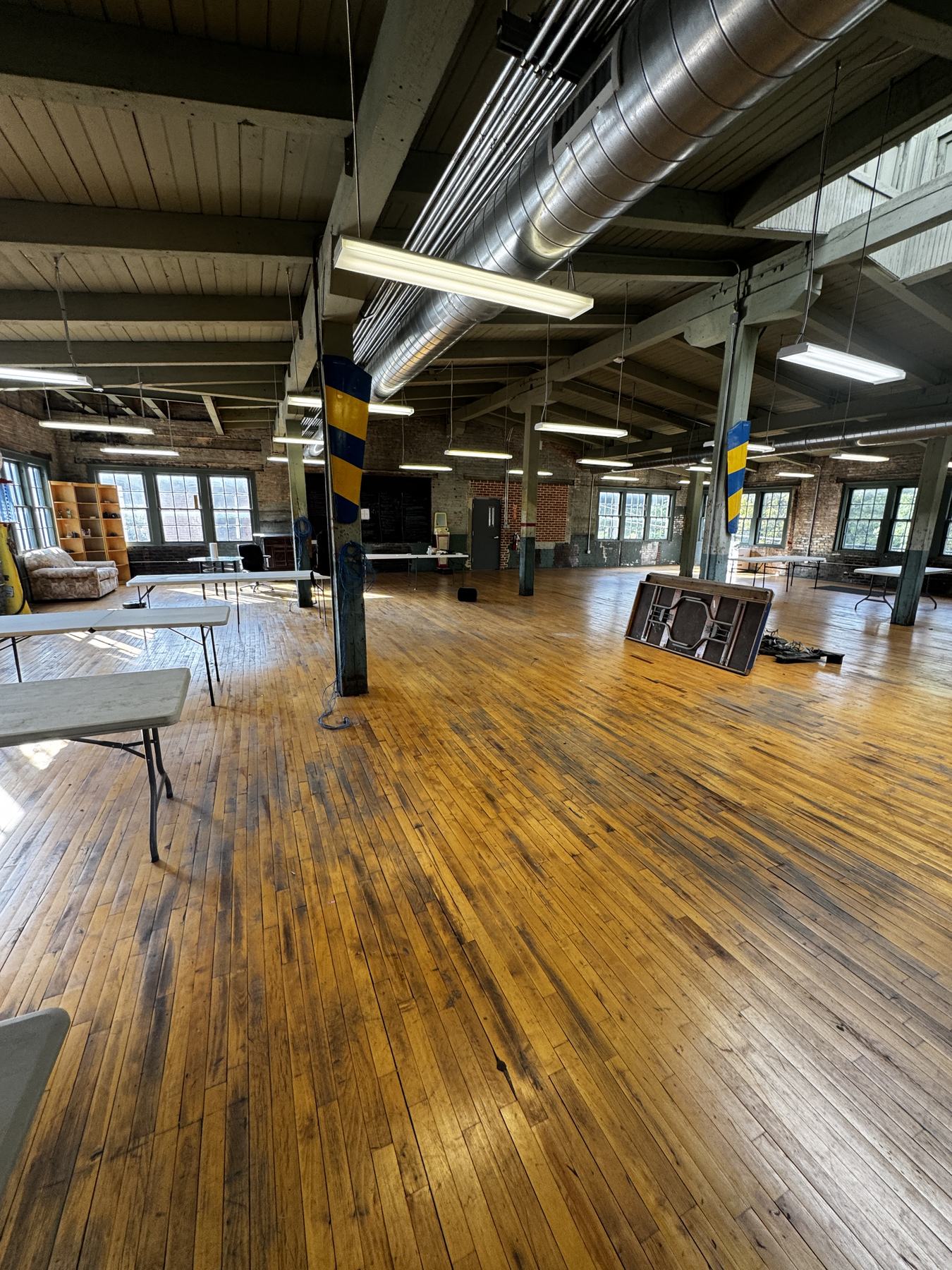 The full depth of the room: beamed ceiling, ductwork, painted timber posts and a run of windows down the far wall.